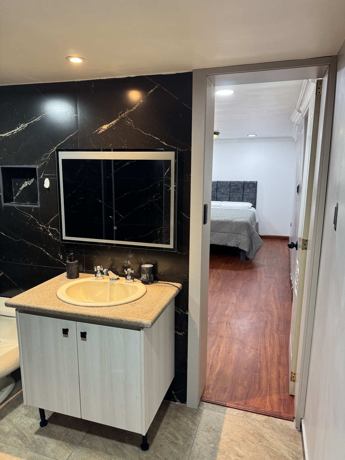 Lavamanos y espejo con vista hacia el dormitorio